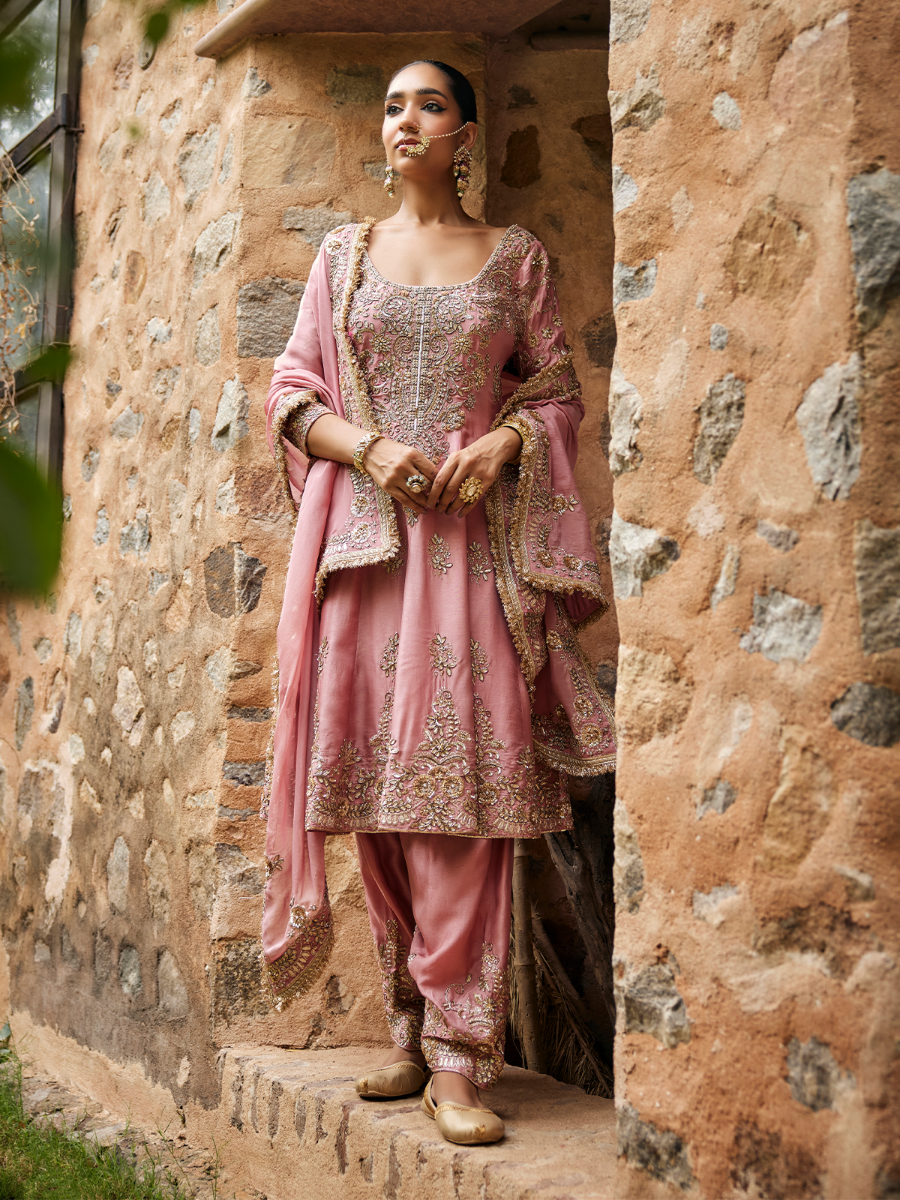 Woman in traditional pink and gold outfit standing in a stone doorway.